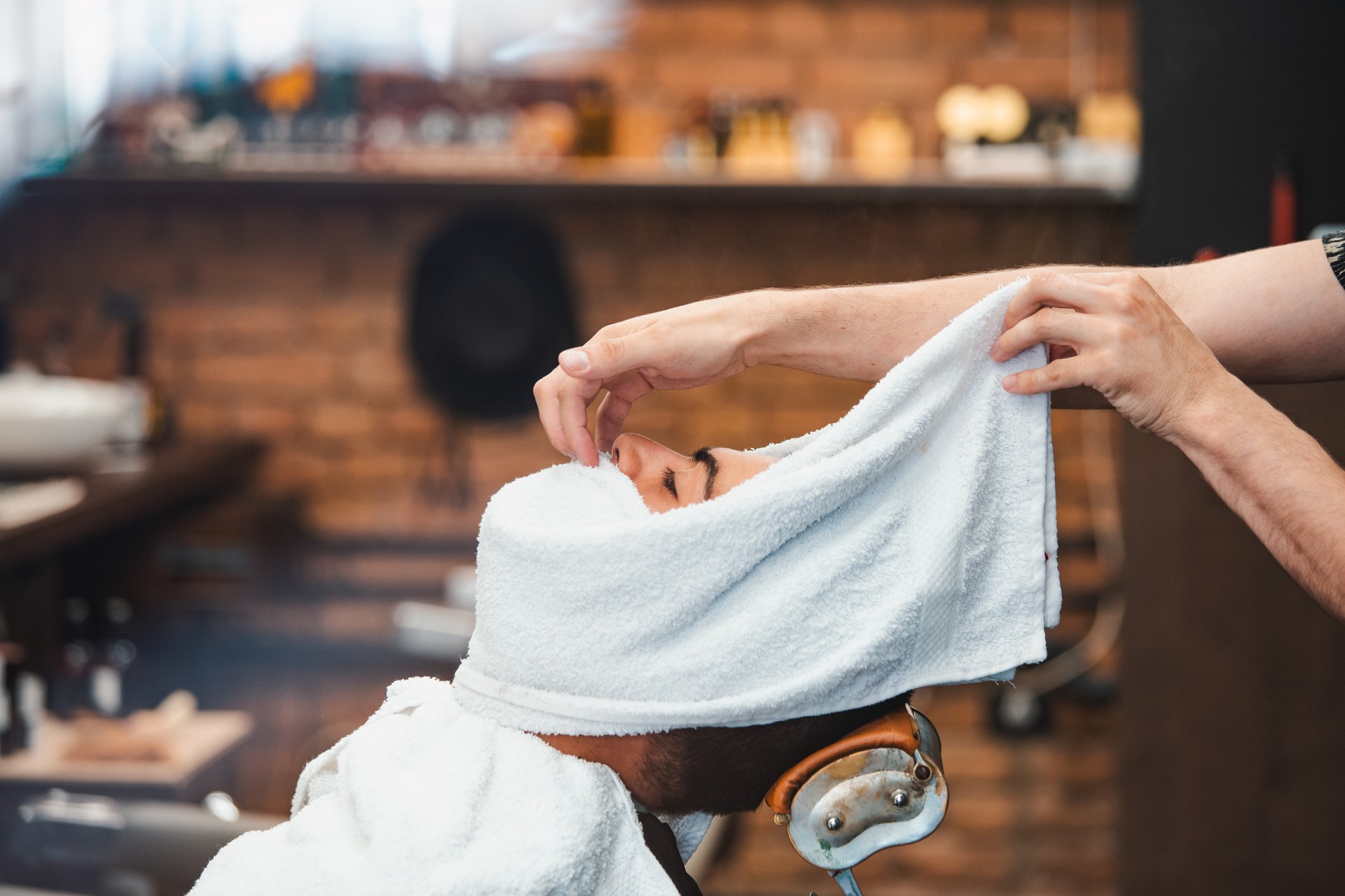 Barber covers the face of a man with a hot towel. Traditional ritual of shaving the beard with hot and cold compresses in a old style barber shop. Client with hot towel on face before shaving in barber shop